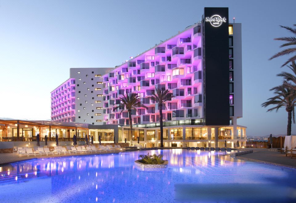 a large hotel with a pink and purple color scheme is surrounded by a pool at Hard Rock Hotel Ibiza