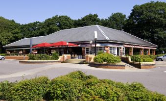 a building with a red awning and multiple umbrellas is surrounded by greenery and bushes at Premier Inn Fareham