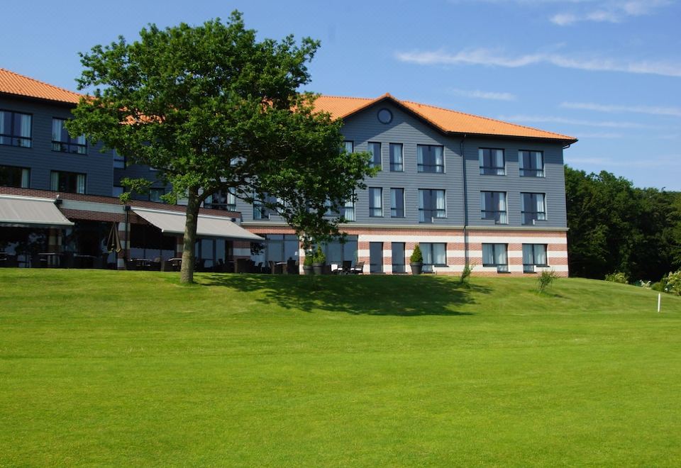 a large , gray and red building with orange roofs is surrounded by a green lawn at Hotel du Golf