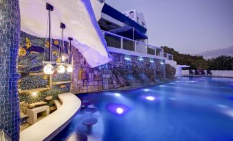 a large outdoor pool with blue water is surrounded by a stone wall and has lights on the side at Vitalis Villas