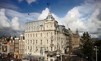 a grand , white building with multiple flags flying on top and a cloudy sky in the background at Park Plaza Victoria Amsterdam