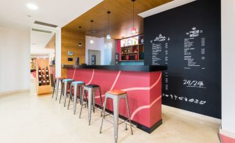 a bar with a red counter and stools , along with a chalkboard menu on the wall at Stay Hotel Guimarães Centro