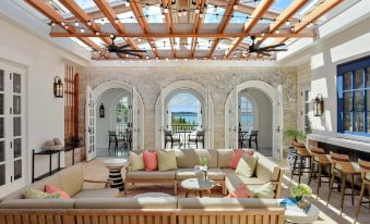 a large , well - lit room with a wooden ceiling and white walls features a couch , chairs , and tables under a ceiling fan at Rosewood Bermuda