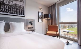 a modern bedroom with a large bed , a chair , and a window overlooking the city at Radisson Hotel Zurich Airport