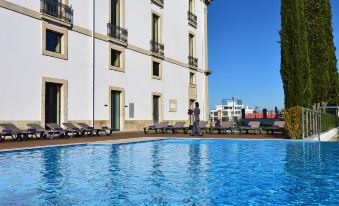 a large swimming pool is located in front of a white building with balconies and people relaxing on lounge chairs at Pousada De Viseu