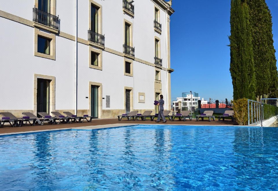 a large outdoor swimming pool surrounded by buildings , with people enjoying their time in the pool at Pousada De Viseu