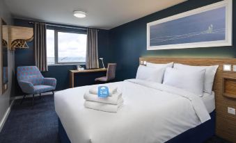 a hotel room with a king - sized bed , a chair , and a window overlooking the ocean at Travelodge Wincanton