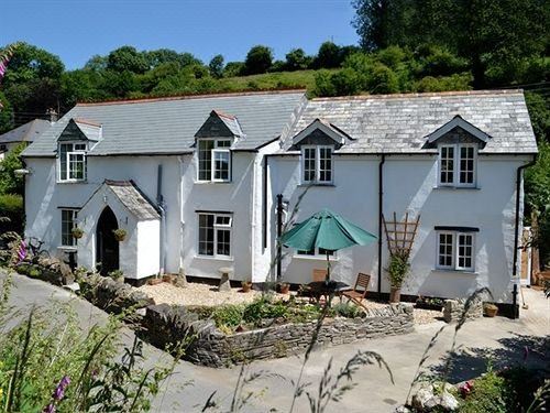 a quaint stone cottage with white walls and black doors , surrounded by greenery and outdoor furniture at The Who'd Have Thought It Inn