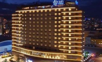 a large hotel with a blue and white logo is lit up at night , surrounded by city lights at Divan Mersin