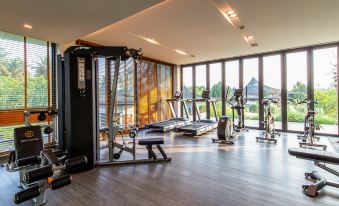 a gym with various exercise equipment , including treadmills and weight machines , near large windows that offer views of the outdoors at Na Tree Tara Riverside Resort Amphawa Damnoensaduak