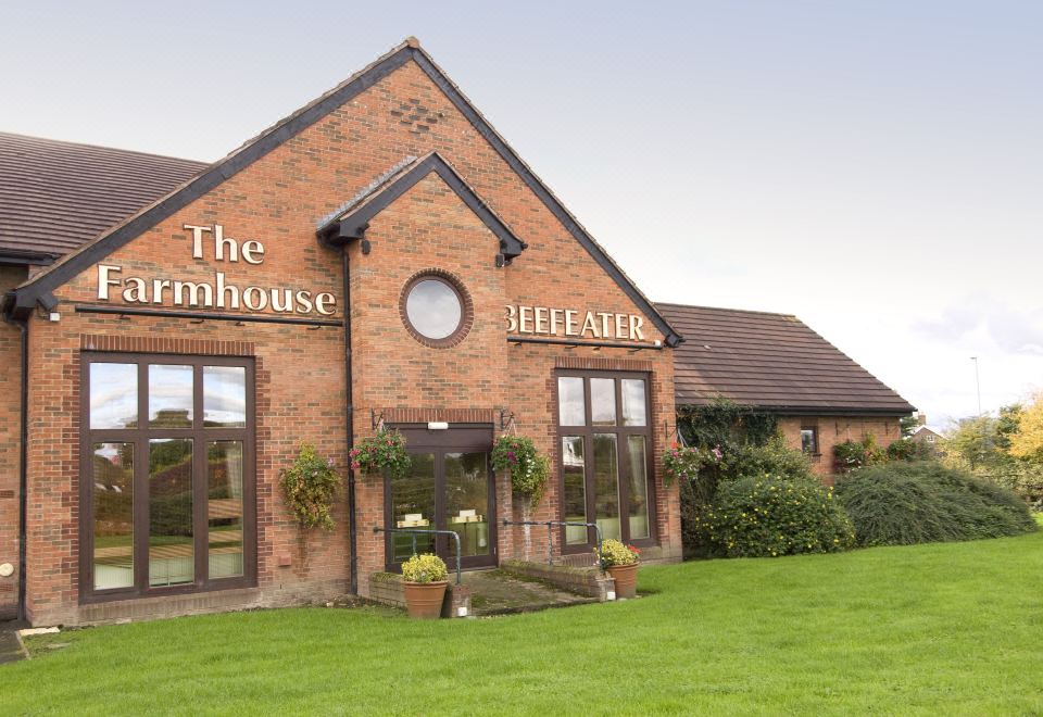 "a brick building with the sign "" the farmhouse "" and a flower garden in front of it" at Crewe West