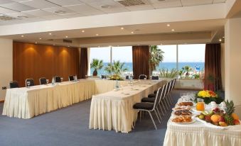 a conference room with a long table , chairs , and a view of the ocean through the windows at Golden Bay Beach Hotel