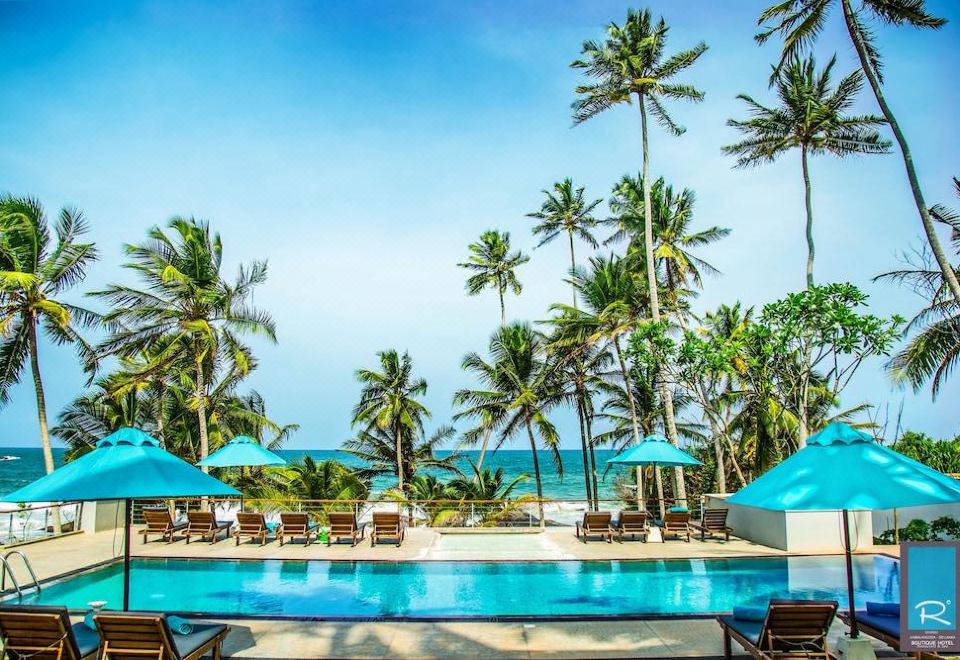 a large swimming pool surrounded by palm trees , with lounge chairs and umbrellas placed around the pool area at R Degrees