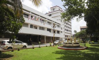 a large white building with multiple balconies and flags on the balconies , surrounded by a lush green lawn and palm trees at Casino Hotels Ltd