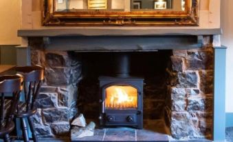 a wood - burning stove with a fire burning in it , surrounded by a stone fireplace and a mirror above at The Exeter Inn