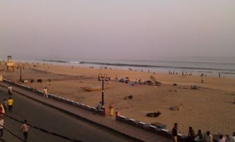 There is a group of people on the beach, with some sitting and others standing, and one person is leaning against an orange object at Hotel Sonali