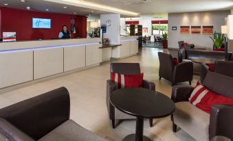 a modern hotel lobby with chairs and tables , a reception desk , and a person behind the counter at London - Dartford