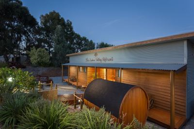 a wooden building with a black tarp covering it , situated in a grassy field near a body of water at The Swan Valley Retreat