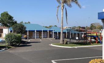 a parking lot with a blue building in the background , and palm trees lining the street at Cameron Thermal Motel