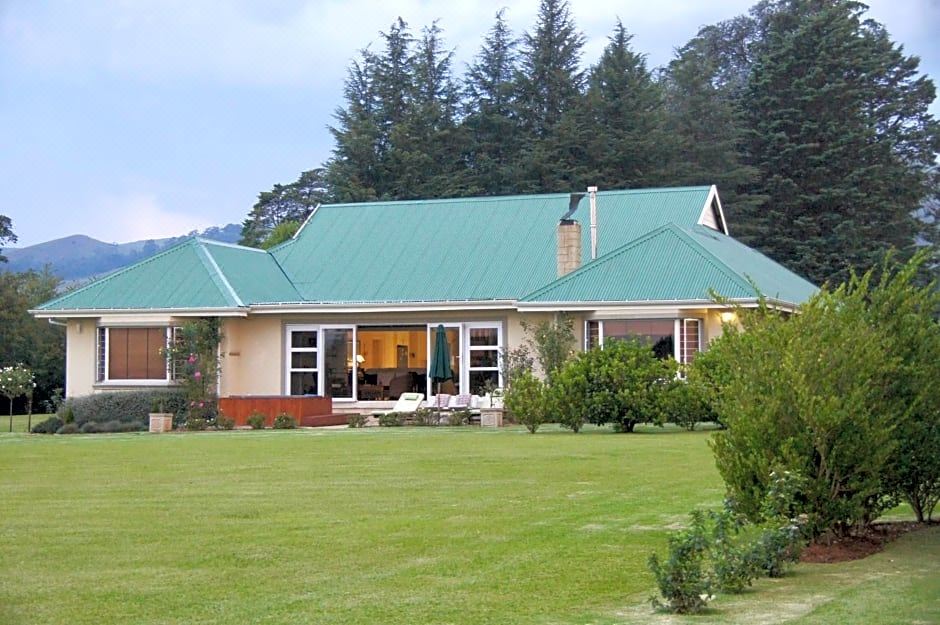 a large house with a green roof and a patio is surrounded by trees and grass at Country Comfort