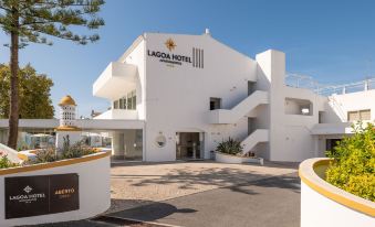 "a modern , white building with the words "" lagoadis hotel "" on its side , surrounded by palm trees" at Lagoa Hotel