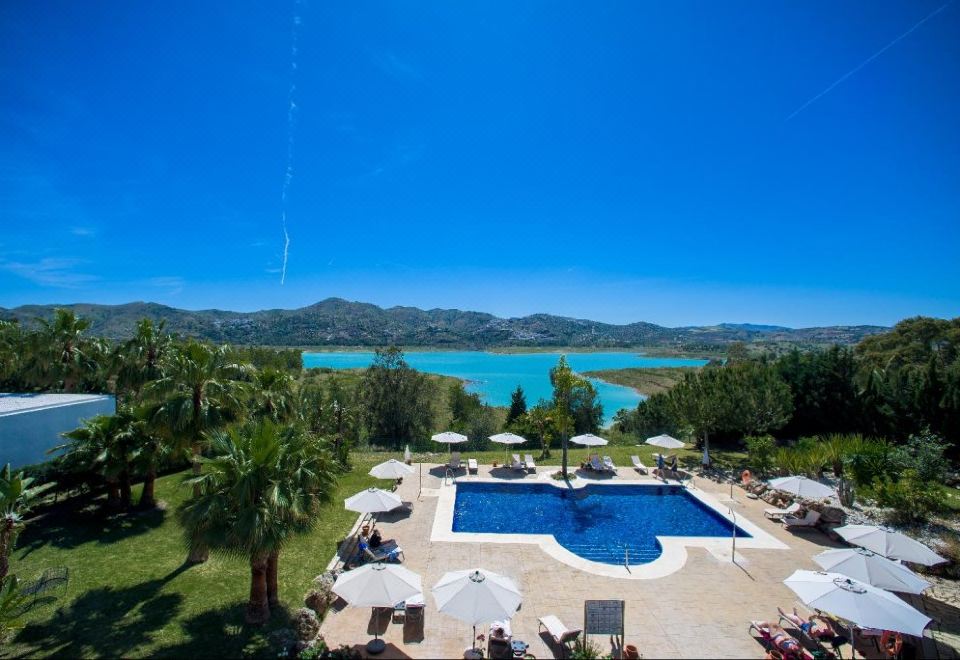 a resort with a large pool surrounded by lounge chairs and umbrellas , as well as a view of a lake and mountains in the distance at B Bou Hotel la Vinuela & Spa