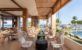 a modern outdoor lounge area with wooden ceiling , white chairs , and black table , overlooking the ocean at Fairmont Mayakoba
