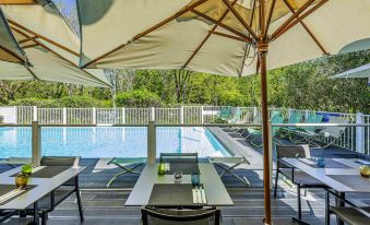 a modern outdoor dining area with umbrellas , tables , and chairs around a pool , set against the backdrop of trees at Novotel Toulouse Centre Compans Caffarelli
