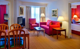 a living room with a red couch , blue chair , and wooden tables , along with lamps and paintings on the walls at Residence Inn Boston Andover