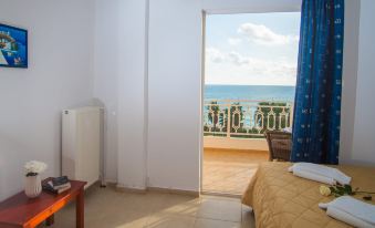 a bedroom with a bed and a door leading to a balcony overlooking the ocean at Poseidon Beach Hotel