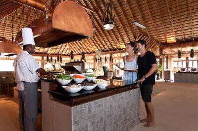 a man and a woman standing in front of a buffet table filled with various food items at Vilamendhoo Island Resort & Spa