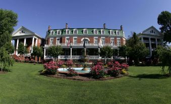 a large , two - story house with a green roof and red accents is surrounded by flowers and greenery at The Martha Washington Inn and Spa