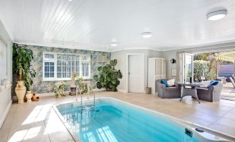 a large swimming pool is surrounded by a living room with a couch and potted plants at The Coast House B&B