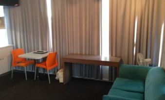 a modern living room with white curtains , blue couches , and orange chairs , as well as a dining area with a table and chairs at Waterfront Lodge Motel