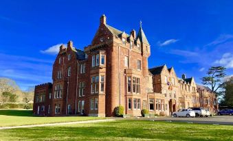 a large red brick building with a green lawn in front of it , under a clear blue sky at Dryburgh Abbey Hotel