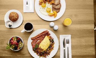a dining table with two plates of food , one containing scrambled eggs and bacon , and the other with other breakfast items at Hilton Garden Inn Falls Church