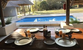 a dining table set for a meal with plates , cups , and utensils , situated next to a pool at Pine Valley Lodge