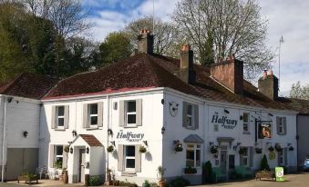 "a large white building with a sign that says "" the halfway pub "" is surrounded by trees and bushes" at Halfway House Inn