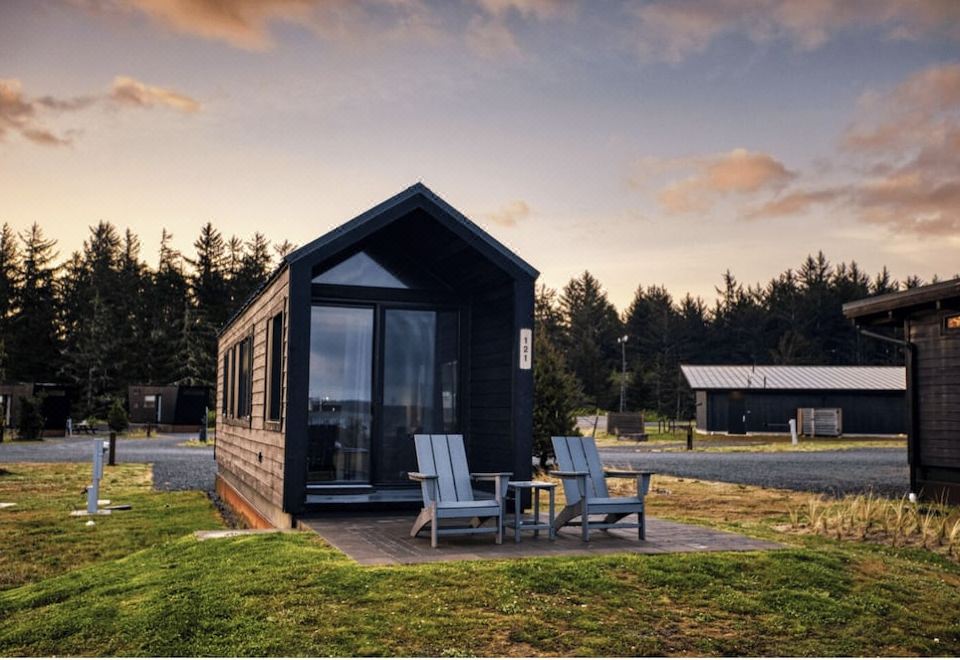 a small black house with a wooden porch and chairs in front of it , surrounded by grass and trees at Bay Point Landing