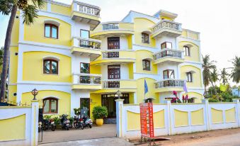a yellow and white building with balconies is surrounded by a white fence and parked motorcycles at OYO Flagship Hotel Priso