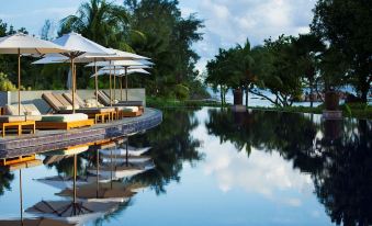 a serene pool area with umbrellas , lounge chairs , and umbrellas , surrounded by lush greenery and a clear blue sky at Raffles Seychelles