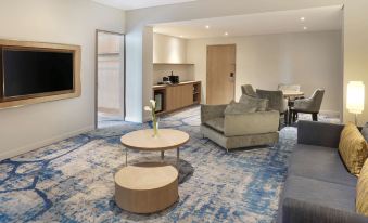 a modern living room with blue and white patterned carpet , a gray couch , wooden coffee table , and two beige chairs at Novotel Jakarta Mangga Dua Square