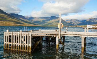a wooden pier extending into a body of water , with mountains in the background and clouds in the sky at Fosshotel Eastfjords