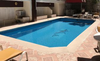 a swimming pool with a blue water and white tiles , surrounded by lounge chairs and an outdoor kitchen at Indiana Hotel