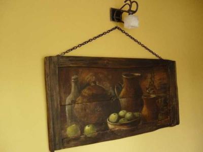 a painting of a vase with fruit is hanging on a wooden frame and a chain is attached to a yellow wall at Troll