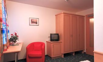 a room with a red chair , wooden cabinet , and television on a table next to a bed at Hotel Post
