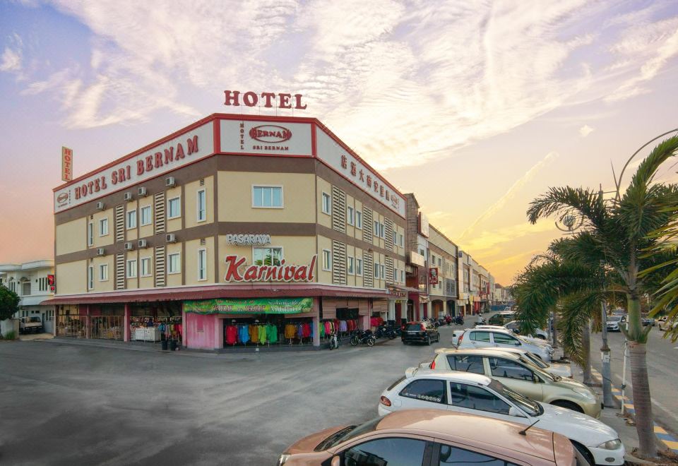 a large hotel with a red sign on the front and several cars parked in front of it at Hotel Sri Bernam