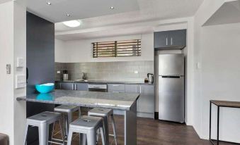 a modern kitchen with stainless steel appliances and a dining table with stools in the background at Azalea Motel