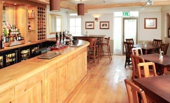 a bar with a wooden counter and chairs , surrounded by chairs and tables in a restaurant setting at The Lamb at Angmering