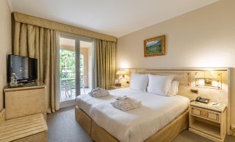 a large bed with white linens and a headboard is in a room with a door leading to a balcony at Hotel Corsica & Spa